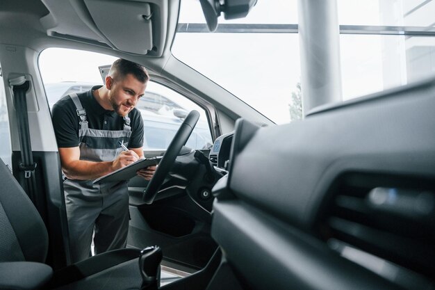 Regardant à l'intérieur de la voiture Un homme en uniforme travaille dans l'autosalon pendant la journée