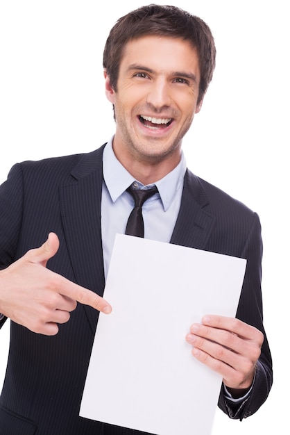 Regarde ça! Heureux jeune homme en tenue de soirée tenant du papier vierge et le pointant avec le sourire