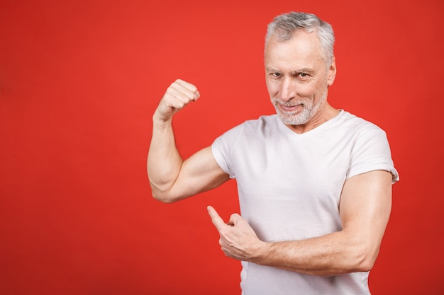 Regarde ça! Homme senior montrant le muscle. Homme âgé fléchissant ses bras isolés. Joyeux excité papy retraité cool moderne pratiquant la musculation.