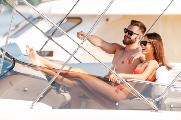 Regarde là-bas! Heureux jeune couple avec impatience avec des sourires alors qu'il était assis sur le bord du yacht