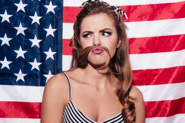 Regarde ma moustache ! Portrait de jeune femme faisant une fausse moustache regarder debout contre le drapeau national américain