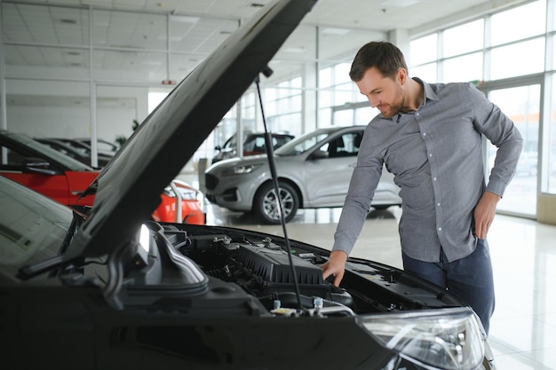 Regarde sous le capot de l'automobile jeune homme dans le concessionnaire automobile