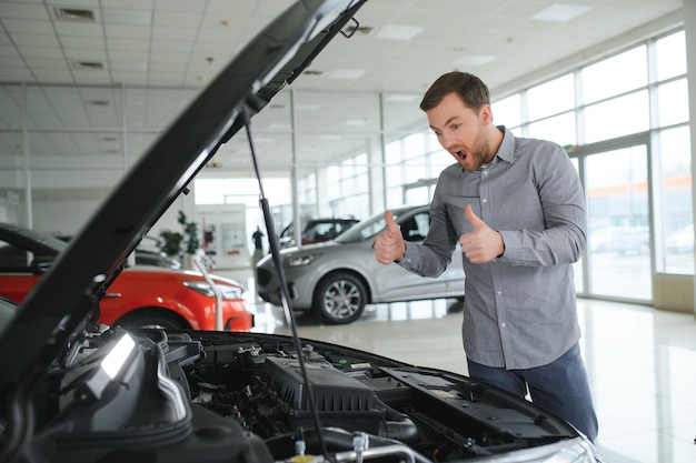 Regarde sous le capot de l'automobile jeune homme dans le concessionnaire automobile