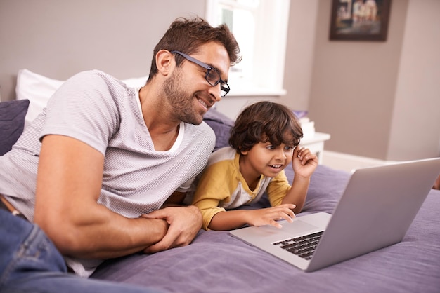 Regarder un film en ligne Photo d'un père et de son fils utilisant un ordinateur portable allongés sur leur lit