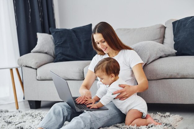 Regarder sur l'ordinateur portable Mère avec sa petite fille est à l'intérieur à la maison ensemble