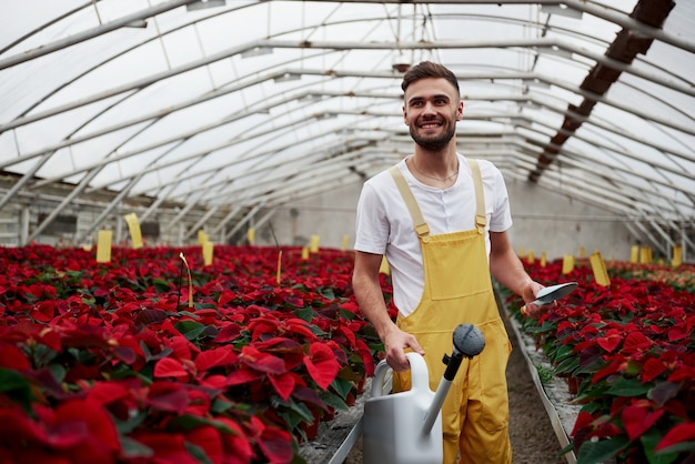 Regarder et sourire. Portrait de beau jeune homme dans la serre en prenant soin des fleurs.