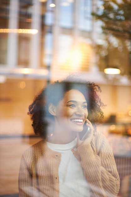 Regardez par la fenêtre une joyeuse femme afro-américaine souriante tout en parlant sur un téléphone portable