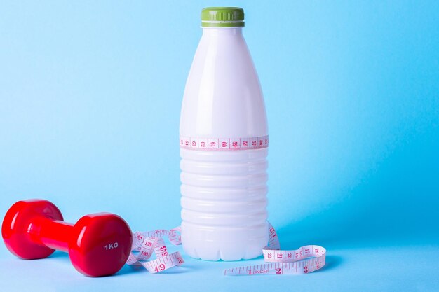 Régime alimentaire minimaliste et concept sportif Bouteille de kéfir haltère rouge ruban à mesurer sur fond bleu