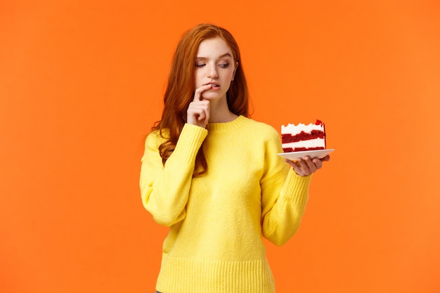 Régime alimentaire, mode de vie sain et concept de malbouffe. Jolie femme rousse ne peut pas résister à la tentation de mordre un délicieux gâteau