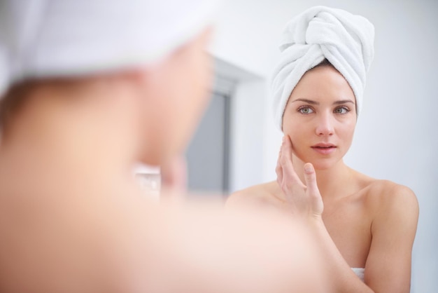 Régime de beauté personnel Une femme regardant dans le miroir de sa salle de bain avec une serviette sur la tête