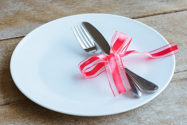 Photo réglage de la table avec assiette, couteau, fourchette, ruban rouge et coeurs sur la table en bois