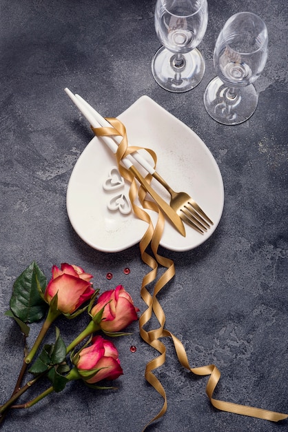 Réglage de la table du dîner romantique avec des roses, des verres de champagne, une assiette en forme de coeur et un ruban doré, la Saint-Valentin ou un dîner romantique