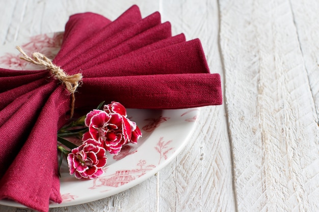 Réglage de la table avec des fleurs d'oeillets et une serviette rouge foncé