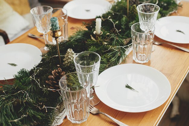 Photo réglage de la table de noël branche de romarin sur assiette bougies de coutellerie vintage branches de sapin avec lumières dorées et pommes de pin sur la table arrangement de vacances atmosphérique