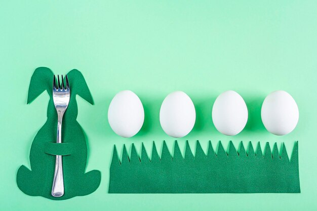 Réglage de la table de Pâques. Porte-couverts créatif drôle mignon en forme de lapin vert et oeufs blancs sur fond vert. Bricolage et créativité des enfants. Fond de Pâques avec espace de copie pour le texte.