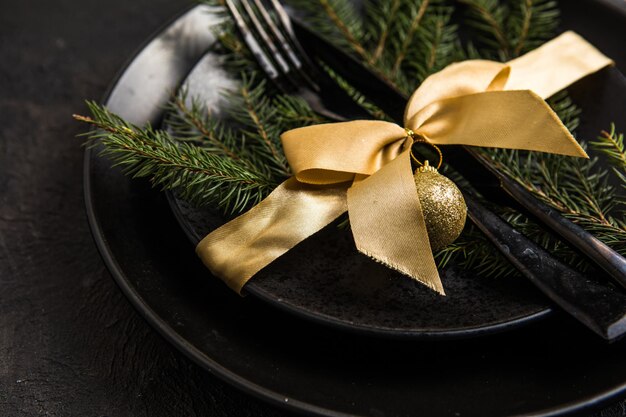 Réglage de la table pour la célébration des vacances de Noël et du nouvel an sur la table. Cadre festif pour le dîner de Noël avec assiette noire et décorations naturelles. Vue de dessus. Espace de copie.