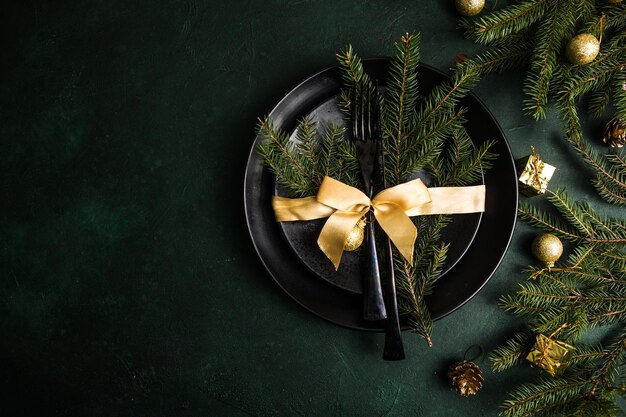 Réglage de la table pour la célébration des vacances de Noël et du nouvel an sur la table. Cadre festif pour le dîner de Noël avec assiette noire et décorations naturelles. Vue de dessus. Espace de copie.