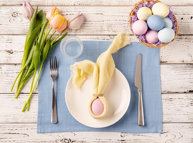 Réglage de la table pour la fête de Pâques Oeufs de Pâques lapin tulipes et couverts vue de dessus à plat sur fond rustique blanc