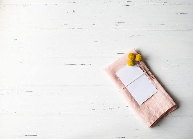 Réglage de la table romantique rustique avec carte en papier, serviette rose, fleurs jaunes sur table en bois blanc. Vue de dessus.