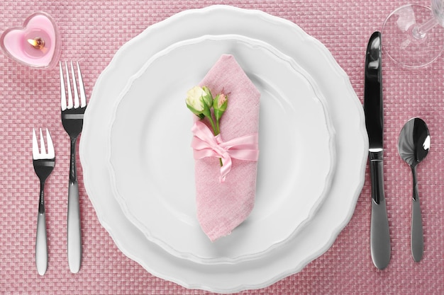 Réglage de la table avec vaisselle, couverts, serviette et bougies sur fond rose