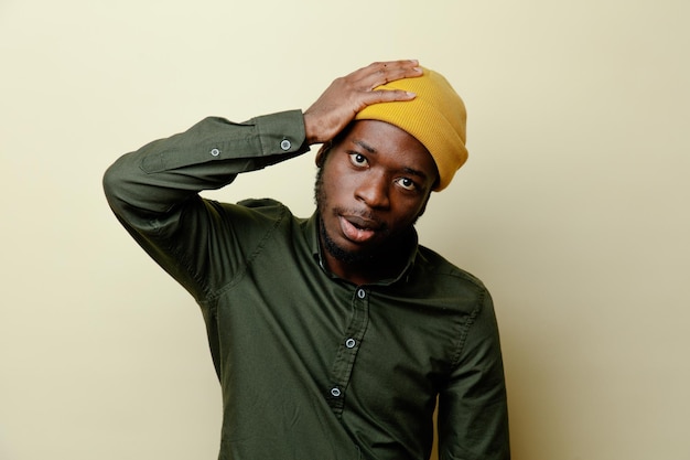 Regret de mettre la main sur la tête a attrapé la tête jeune homme afro-américain au chapeau portant une chemise verte isolée sur fond blanc