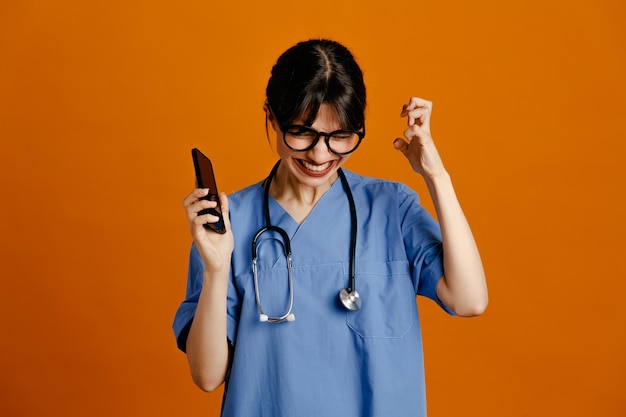 Regret tenant le téléphone jeune femme médecin portant un stéthoscope fith uniforme isolé sur fond orange