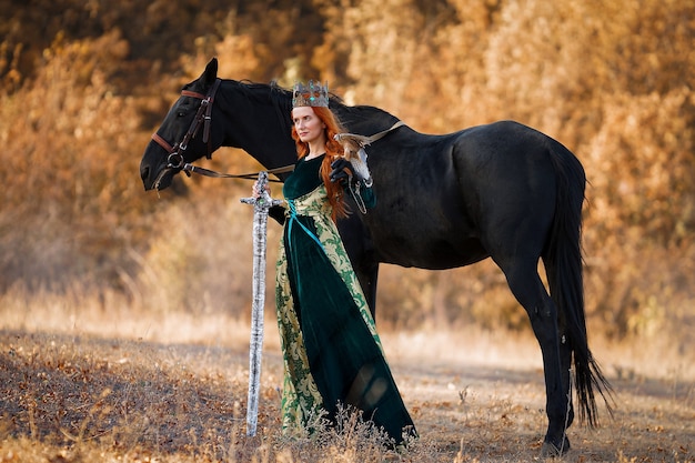 Reine aux cheveux rouges dans une robe verte avec une couronne et une épée près d'un cheval avec un oiseau