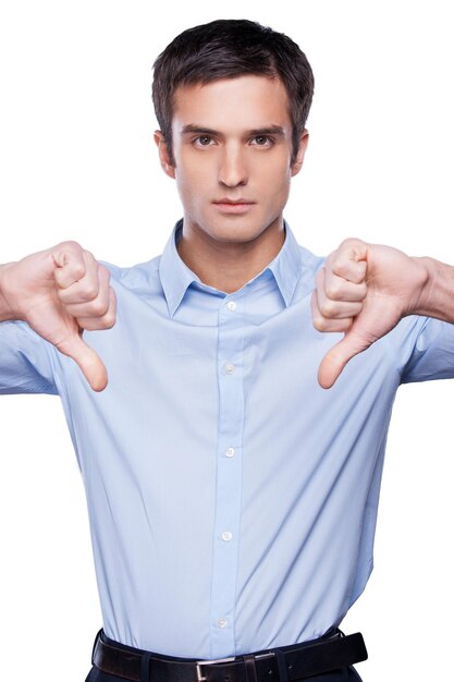 Rejeté! Jeune homme sérieux en chemise bleue montrant ses pouces vers le bas et regardant la caméra en se tenant debout isolé sur blanc