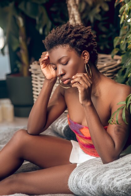 Relaxation. Jeune femme à la peau sombre dans un haut brillant et un short blanc à la réflexion