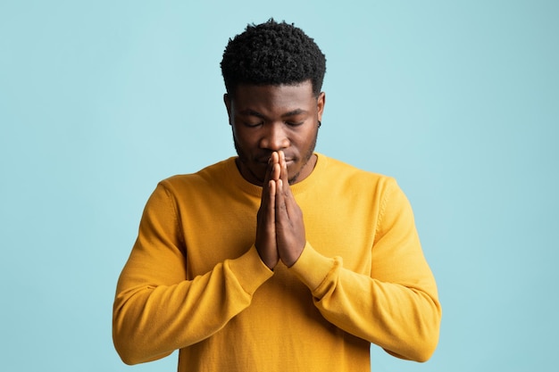 Religieux jeune homme afro-américain priant sur bleu