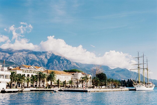 Remblai de Tivat avec des maisons en pierre et un voilier blanc amarré au Monténégro