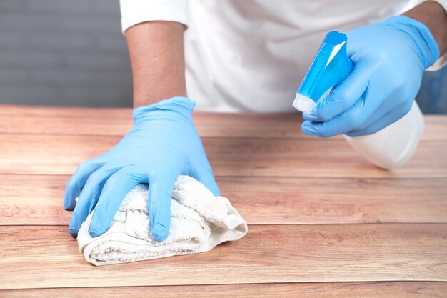 remettre des gants jetables à l'aide d'un spray désinfectant pour nettoyer la surface de la table