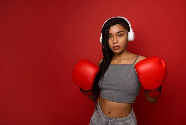 Remise en forme jeune boxeuse afro-américaine avec un corps en forme se préparant à l'entraînement de boxe. Autodéfense des femmes. Concept d'entraînement cardio sur fond de couleur rouge avec espace de copie pour la publicité