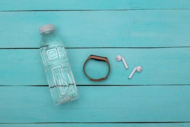 Photo remise en forme, sport minimaliste à plat. bouteille d'eau, écouteurs sans fil et bracelet intelligent sur fond de bois bleu. vue de dessus