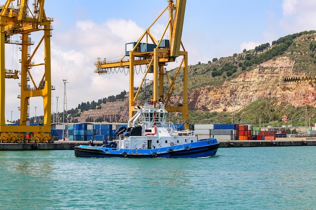 Remorqueur dans le port de Barcelone avec de grandes grues de déchargement de conteneurs.