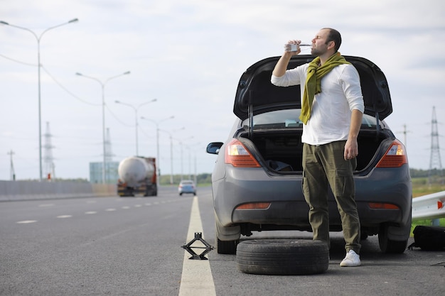 Remplacement de la roue d'une voiture sur la route. Un homme travaillant sur les pneus en marge.