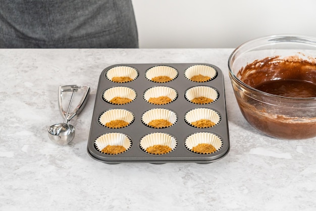 Remplir des moules à cupcakes en aluminium avec une pâte à cupcakes au chocolat pour cuire des cupcakes s'mores.