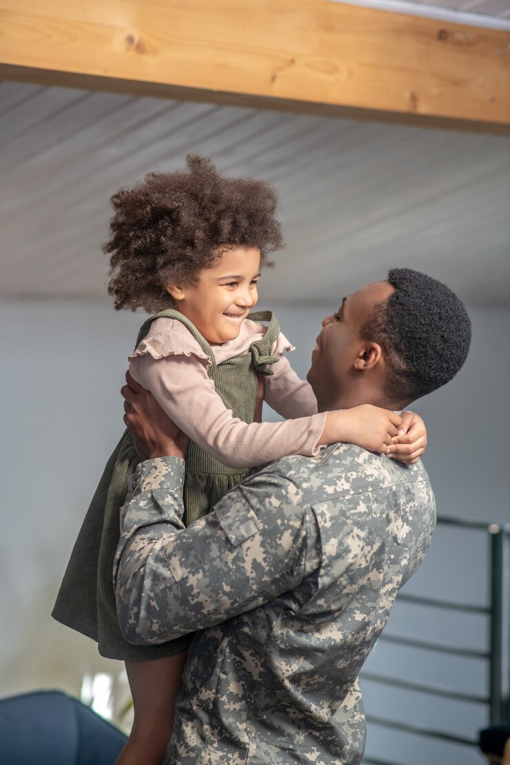 Rencontre tant attendue. Jeune papa fort à la peau foncée en uniforme militaire tenant une petite fille brillante aux cheveux bouclés se réjouissant de la réunion