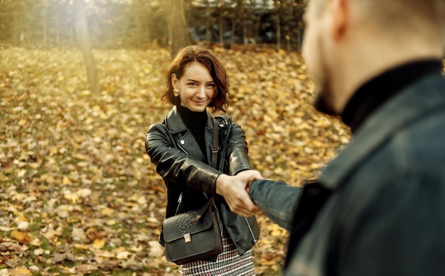 Un rendez-vous romantique. Un jeune couple d'amoureux s'amuser se tenant la main sur le fond des feuilles d'automne tombées. Suis-moi