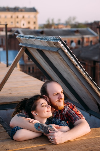 Rendez-vous romantique sur le toit. Couple profitant du coucher du soleil. Des relations tendres, des gens heureux au premier plan. Agréable moment ensemble au sommet du monde, fond urbain