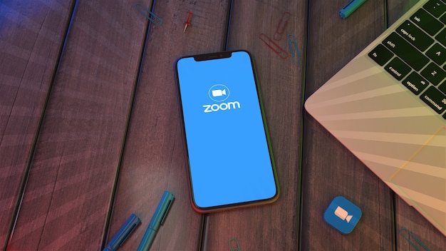 Rendu 3D d'un smartphone affichant le logo de l'application Zoom sur un bureau en bois