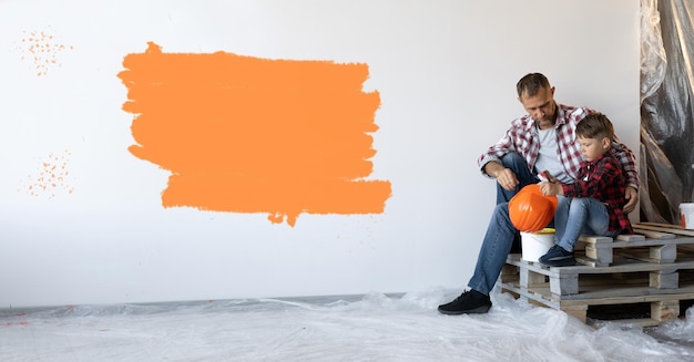 réparant sa maison et le fils est assis près du mur avec une tache orange Baner Copy space