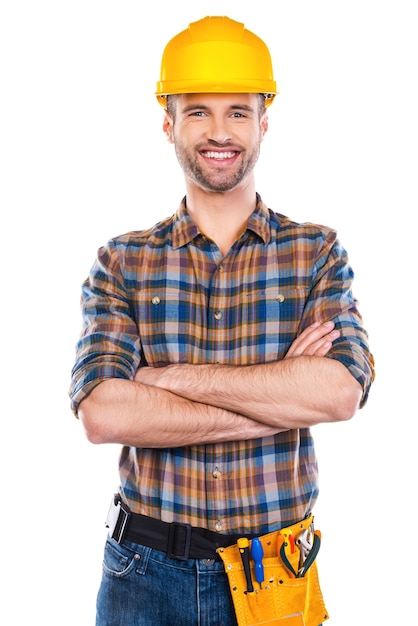 Réparateur confiant. Confiant jeune homme charpentier en casque gardant les bras croisés et souriant en se tenant debout sur fond blanc