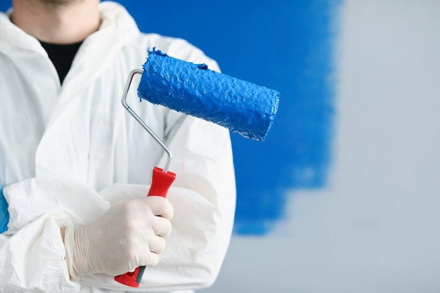 Réparateur de constructeur d'homme tenant un rouleau avec de la peinture bleue dans ses mains en gros plan