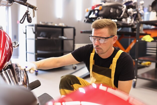 Réparateur d'homme dans des lunettes ramassant la peinture à la moto dans la réparation et l'atelier de réparation de voiture