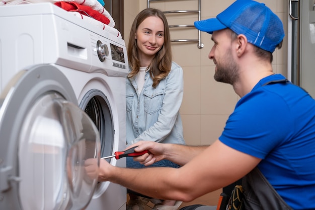 Réparateur répare une machine à laver devant une femme un homme communique avec le propriétaire d'une machine à laver