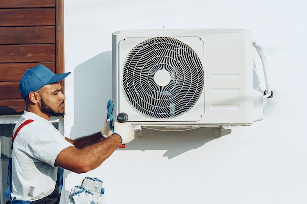 Réparateur en uniforme installant l'unité extérieure du climatiseur