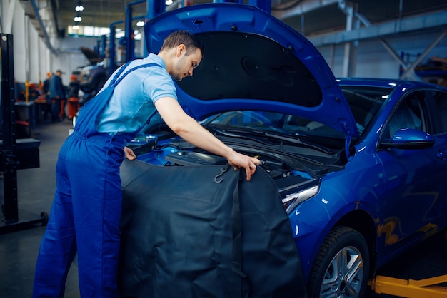 Réparateur en uniforme vérifie le moteur du véhicule, la station-service de voiture. Contrôle et inspection automobile, diagnostic et réparation professionnels