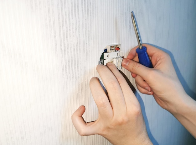 Réparation d'électriciens Installation de la prise avec un tournevis dans un mur en béton après avoir posé du papier peint