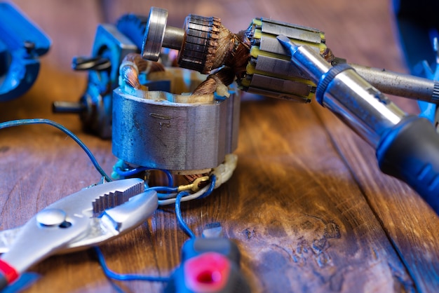 Réparation d'outils électriques. Détails d'un appareil électrique et d'outils de réparation sur une table en bois dans un atelier de réparation. Un contremaître répare un outil électrique à l'aide d'un fer à souder et d'une pince